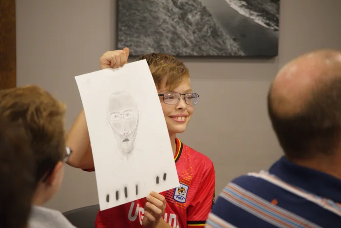 A boy holding up a portrait he drew.