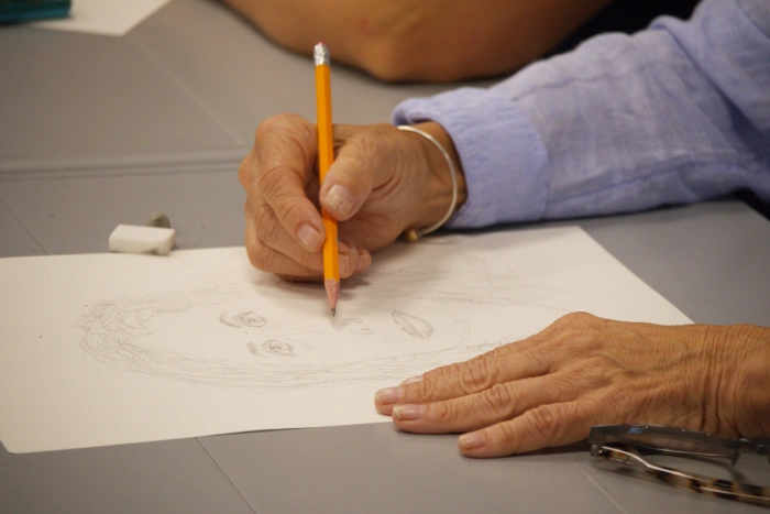 A women drawing a portrait of another with pencil.