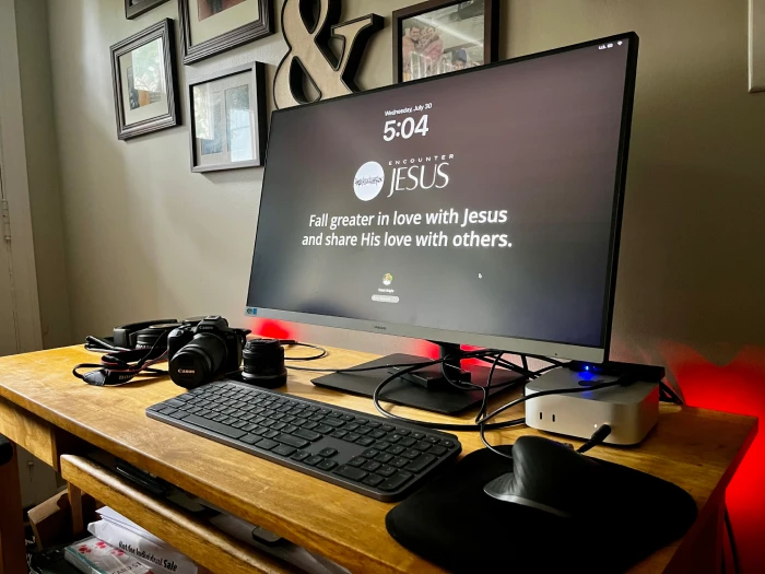 A desk with a computer, camera, headphones, and other things.
