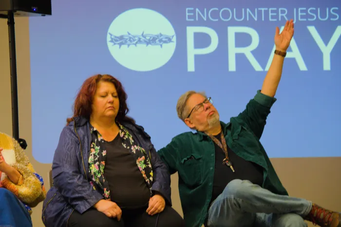 A couple at Encounter Jesus Prayer before service - man is raising his hand.