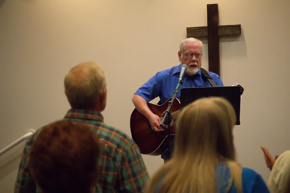 A man playing an acoustic guitar and people worshiping Jesus.